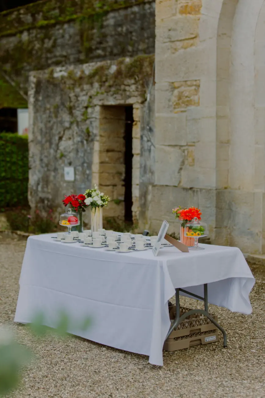 Table de réception avec nappe blanche, fleurs fraîches et cadeaux d'invités installée devant un mur en pierre ancienne lors d'un mariage.