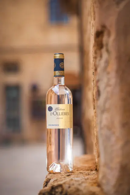 Bouteille de vin rosé Château d'Ollières Classique 2025 posée sur un muret en pierre typique d'un village de Provence.