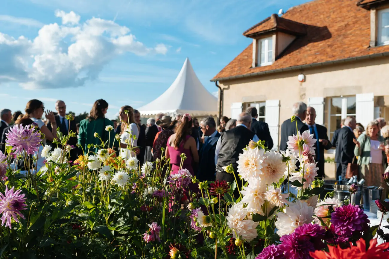 Réception de mariage champêtre en extérieur avec buffet de rafraîchissements et invités devant une maison de caractère.