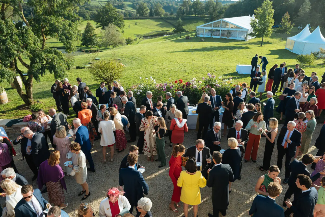Vin d'honneur de mariage en extérieur avec invités dégustant du vin devant un chapiteau de réception.