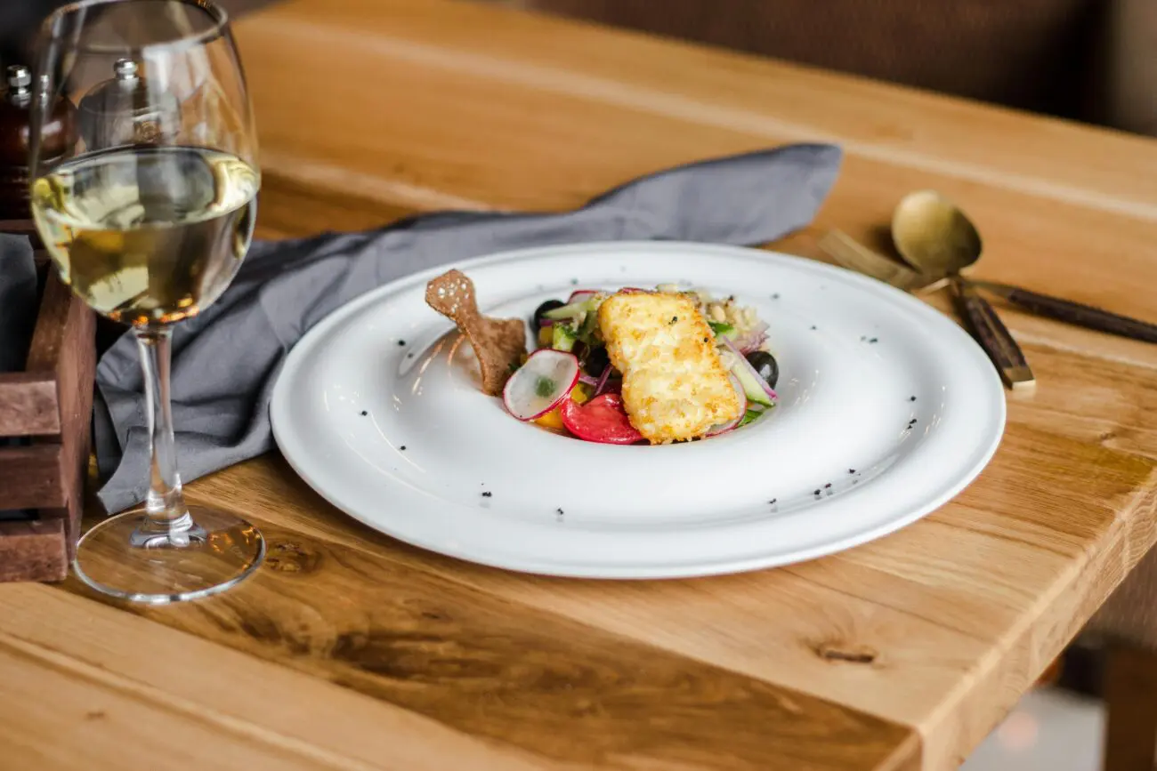 Accord mets-vins de mariage : entrée gastronomique servie dans une assiette blanche design, accompagnée d'un verre de vin blanc frais sur une table en bois clair.