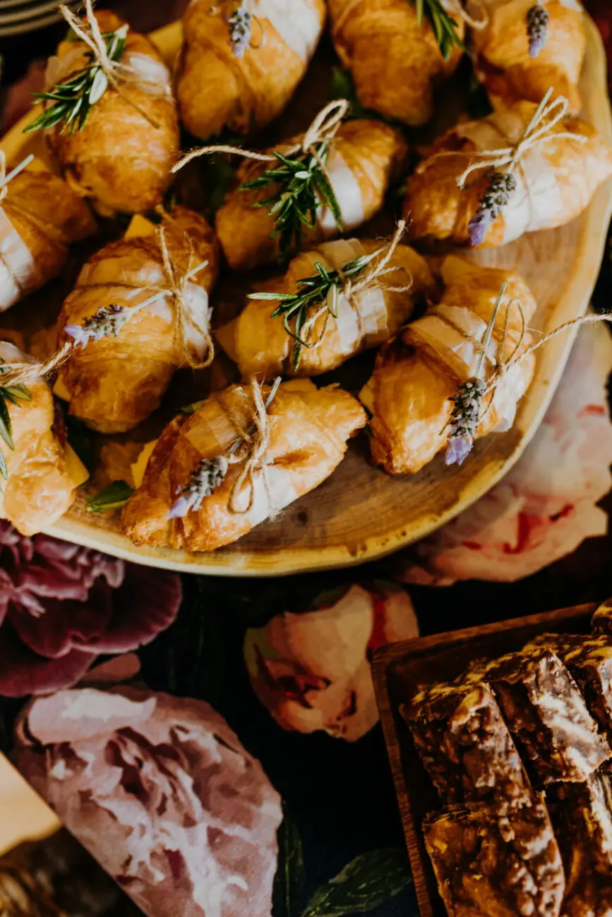 Mini-croissants salés décorés de romarin et lavande sur un plateau en bois pour un brunch de mariage, un accord mets-vins signé vins-mariages.net.