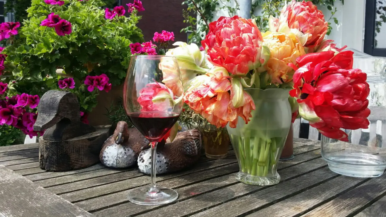 Un verre de vin rouge posé sur une table en bois rustique à côté d'un bouquet de tulipes rouges et orangées dans un jardin.
