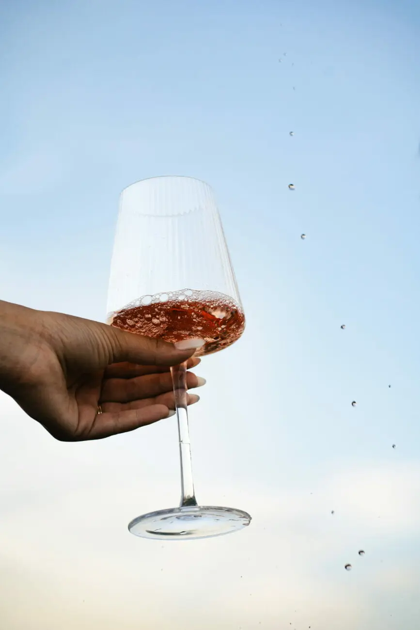 Main tenant un verre de vin rosé levé vers le ciel pour un toast lors d'un mariage, sélectionné par vins-mariages.net.