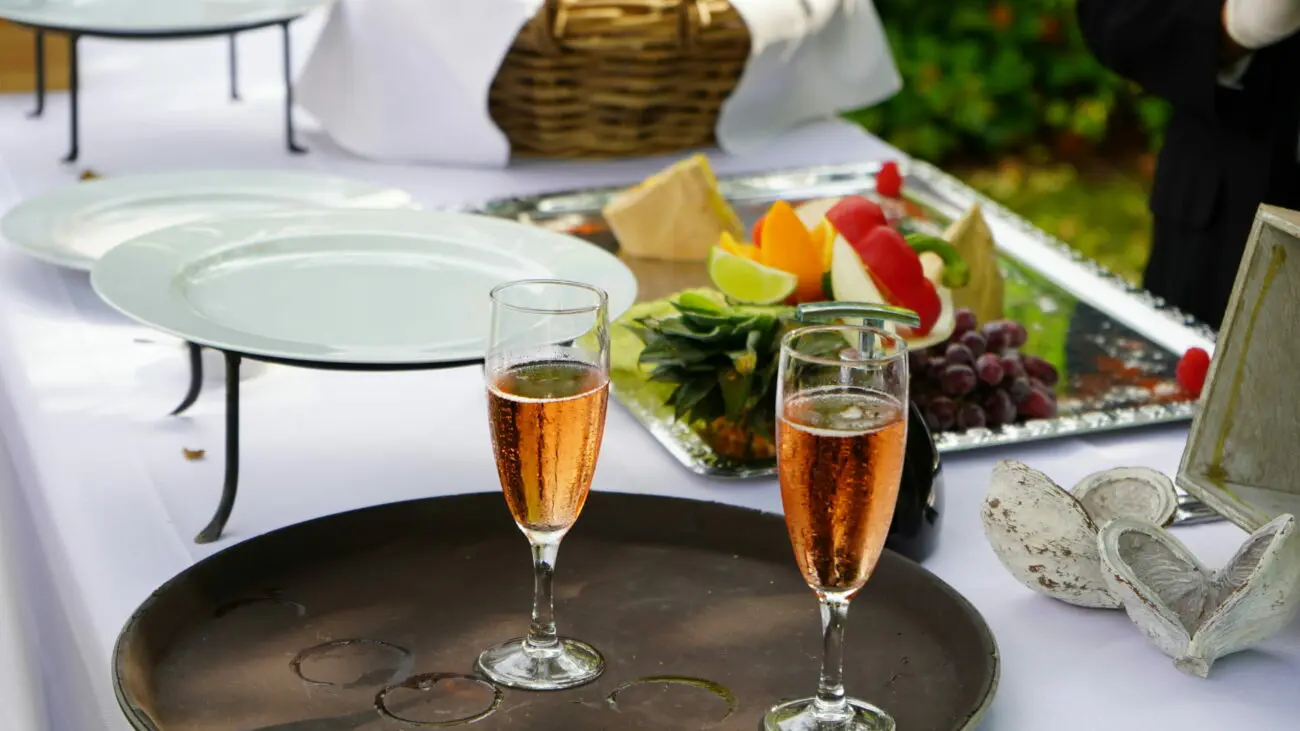 Deux flûtes de vin rosé pétillant sur un plateau, devant un buffet de brunch de mariage avec fruits frais, proposé par vins-mariages.net.