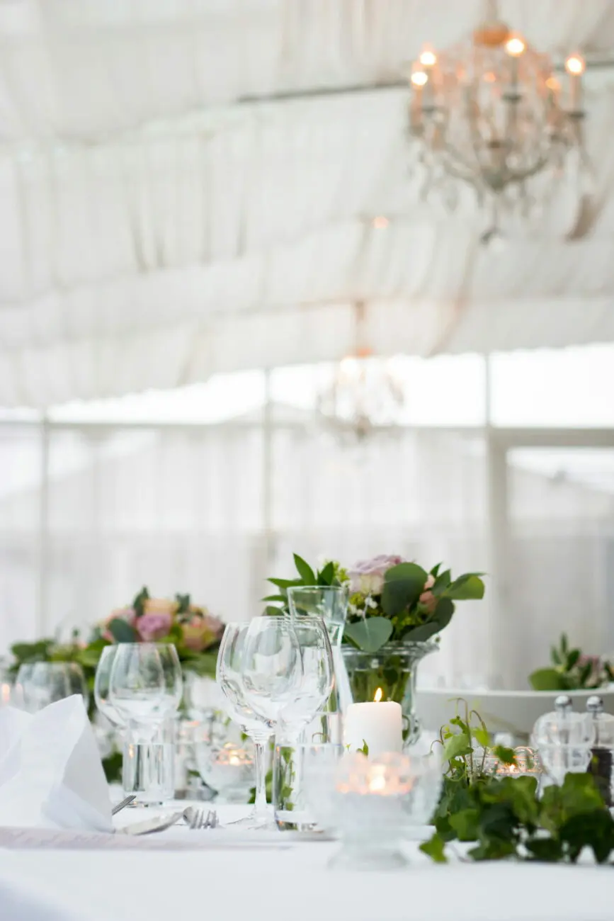 Décoration de table de mariage élégante avec verres à vin cristallins, fleurs et bougies sous un chapiteau par vins-mariages.net