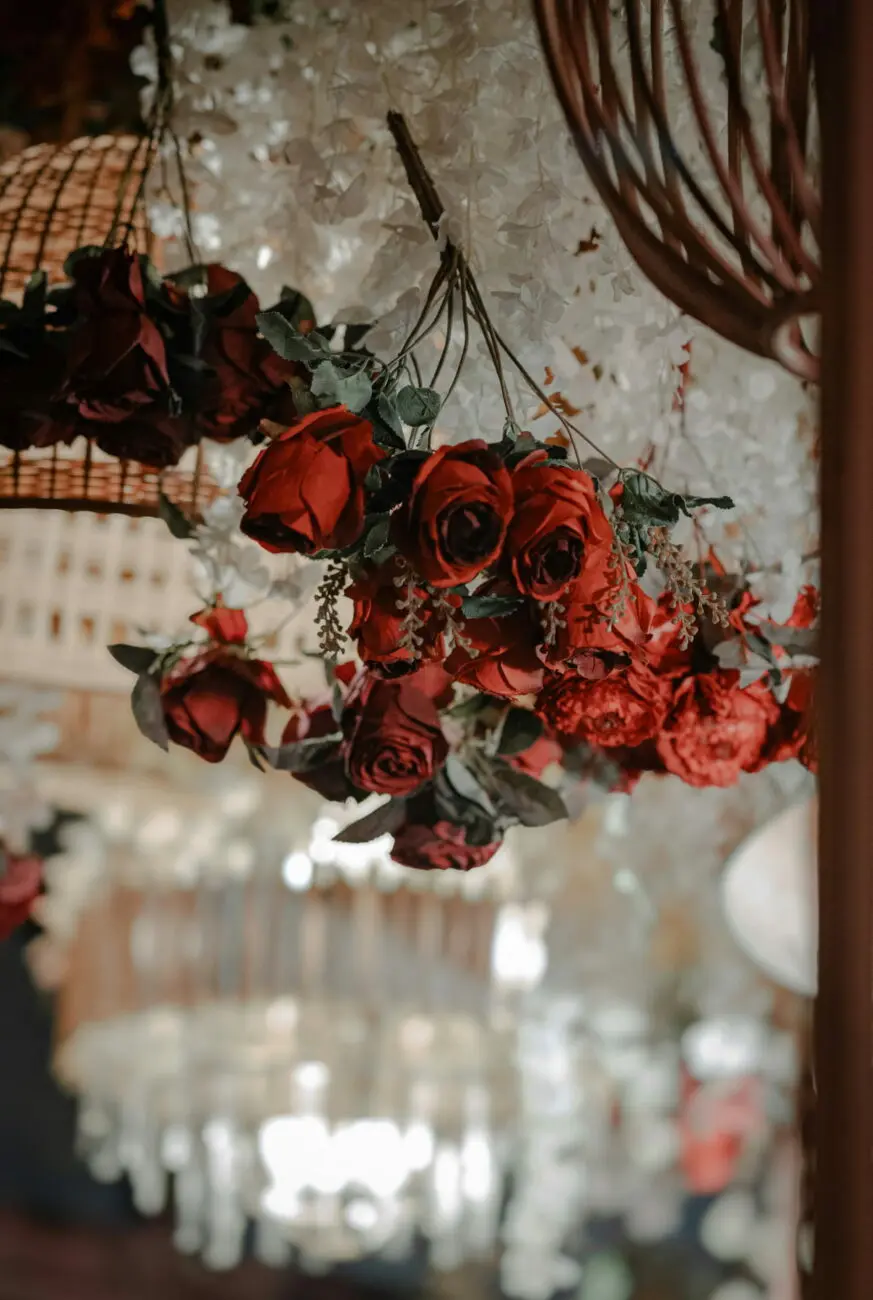 Suspension de roses rouges et fleurs blanches avec lustre en cristal en arrière-plan pour une décoration de salle de mariage élégante.