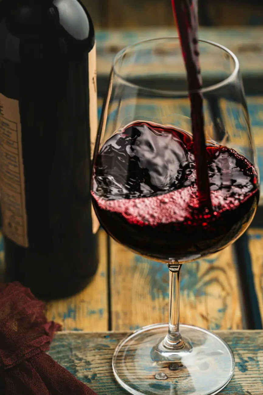 Gros plan sur un vin rouge intense versé dans un grand verre à dégustation posé sur une table en bois bleu vieilli.