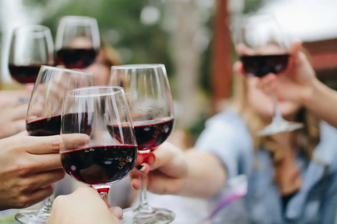 Plusieurs mains d'invités portant un toast avec des verres de vin rouge lors d'une réception de mariage en plein air.