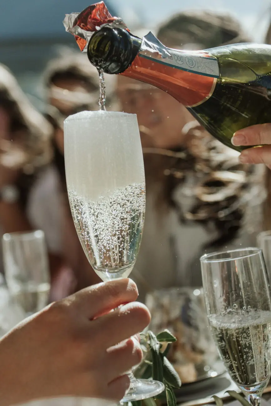 Gros plan sur une bouteille de champagne versant des bulles dans une flûte lors d'une réception de mariage en plein air.