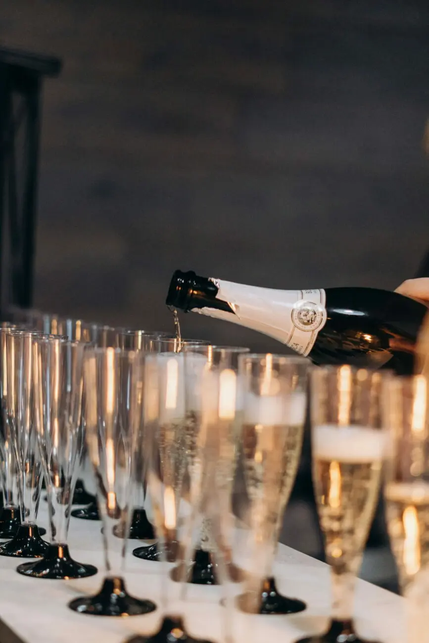 Un serveur remplit une rangée de flûtes à champagne élégantes lors d'une réception de mariage.