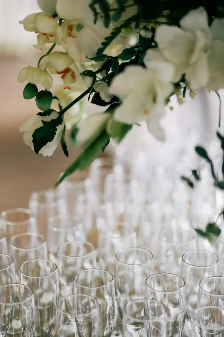 Alignement de flûtes à champagne vides sur une table de réception de mariage avec une décoration de fleurs blanches au premier plan.