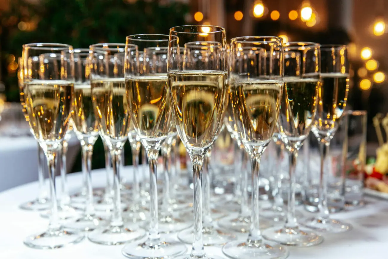 Alignement de flûtes de champagne et de vins pétillants sur un buffet de mariage éclairé, une sélection vins-mariages.net.