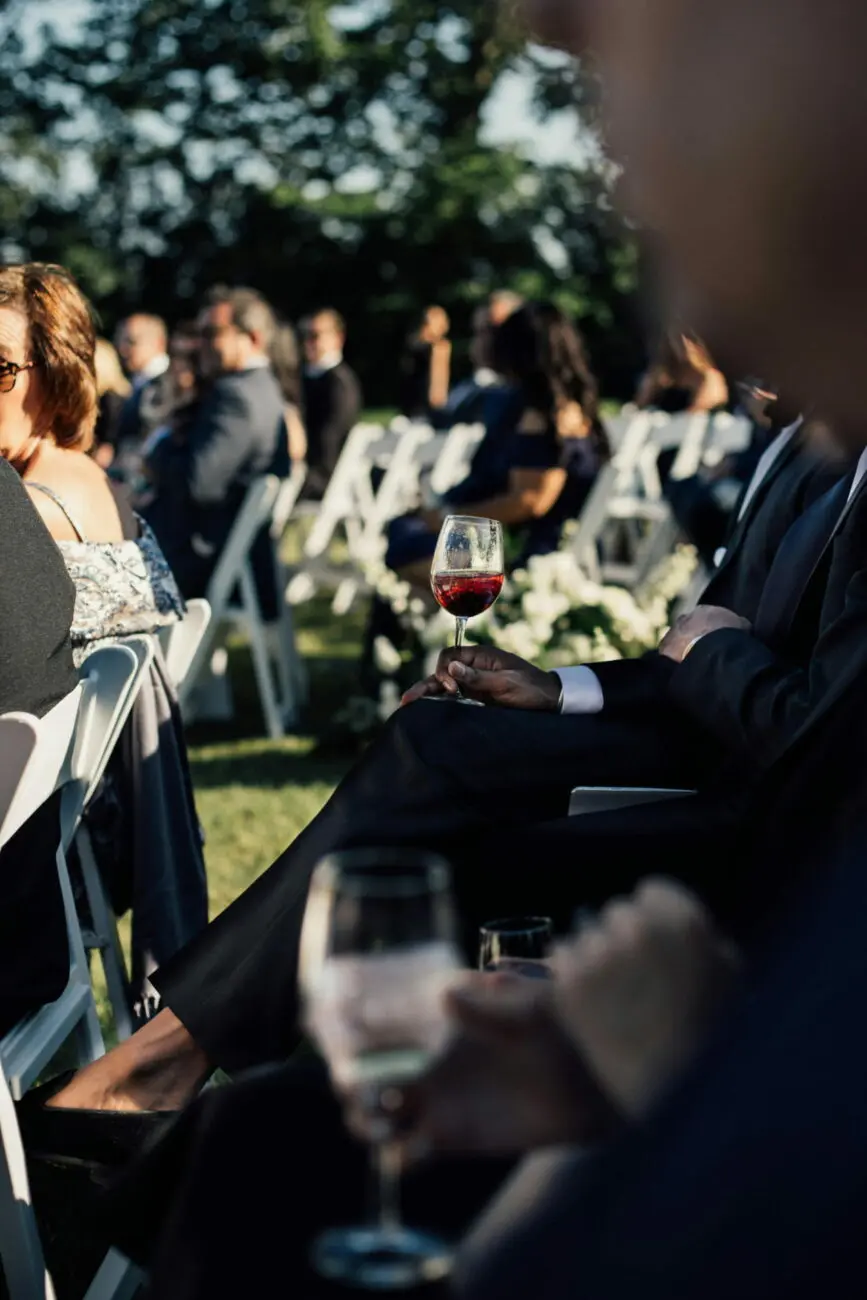 Invité tenant un verre de vin rouge lors d'une cérémonie de mariage en extérieur, servi par vins-mariages.net.