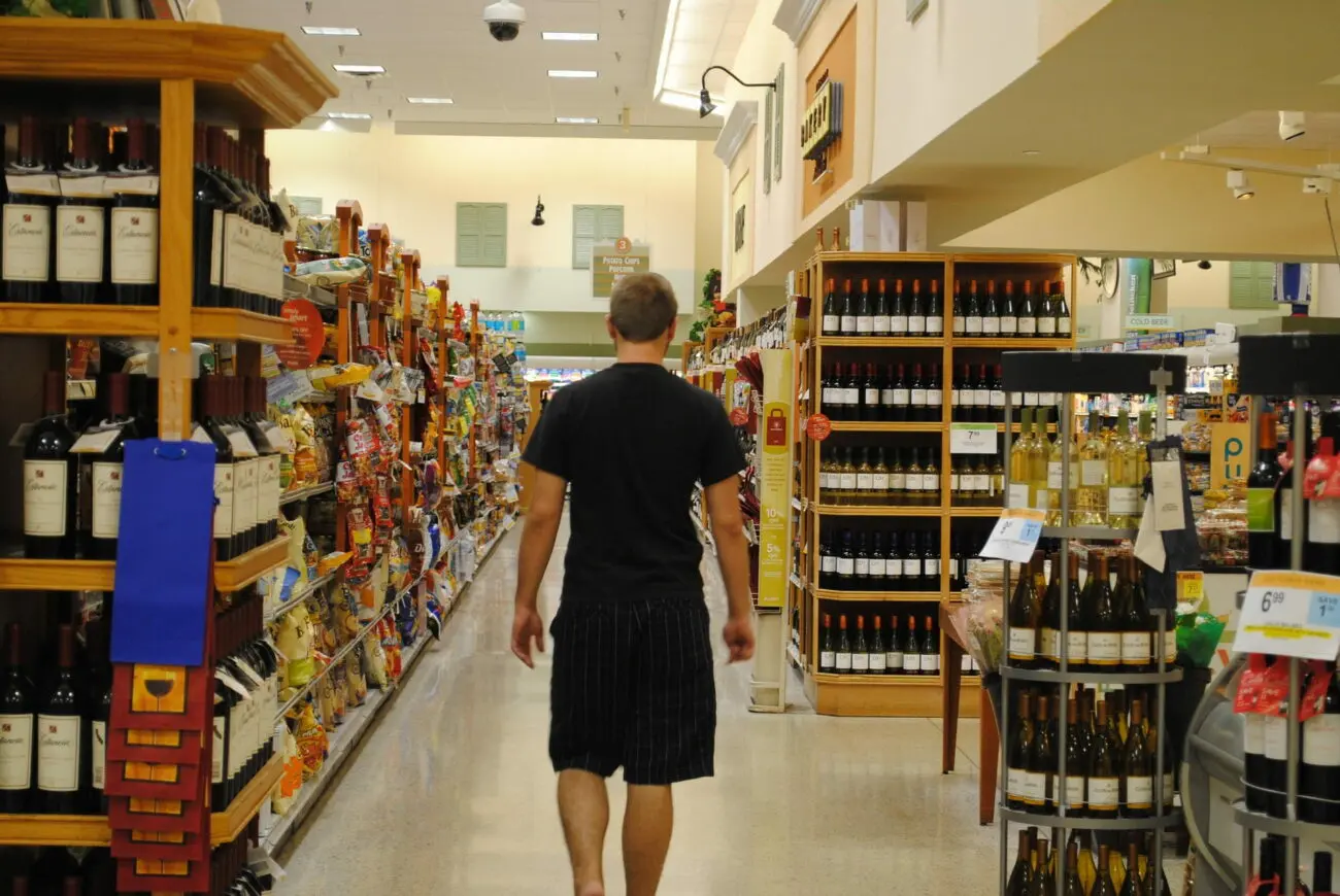 Homme de dos marchant dans le rayon vin d'un supermarché de la grande distribution.
