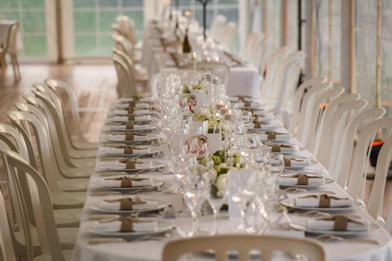 Longue table de banquet de mariage dressée avec verres à vin, prête pour le service d'une sélection personnalisée.