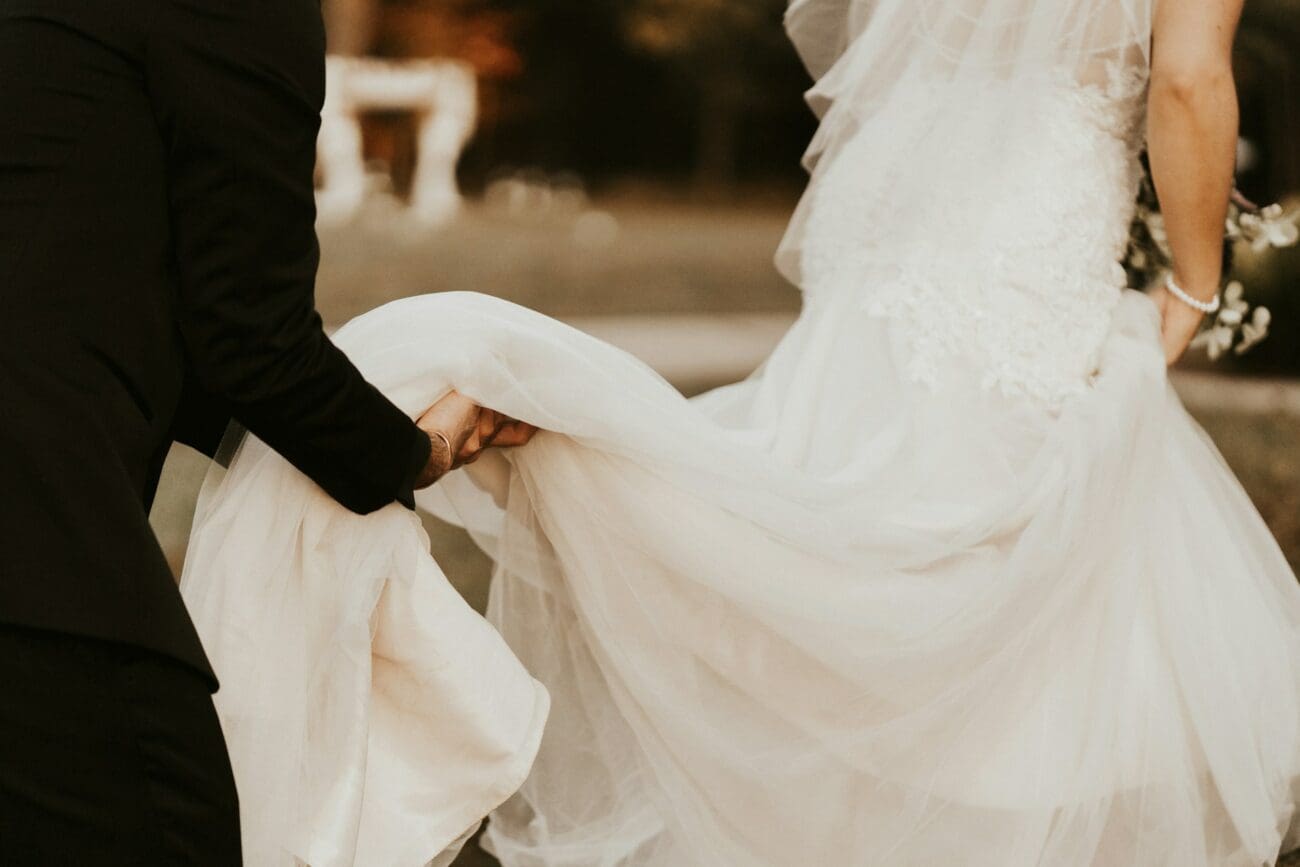 Marié aidant la mariée en soulevant la traîne de sa robe blanche en dentelle lors d'un moment de complicité.