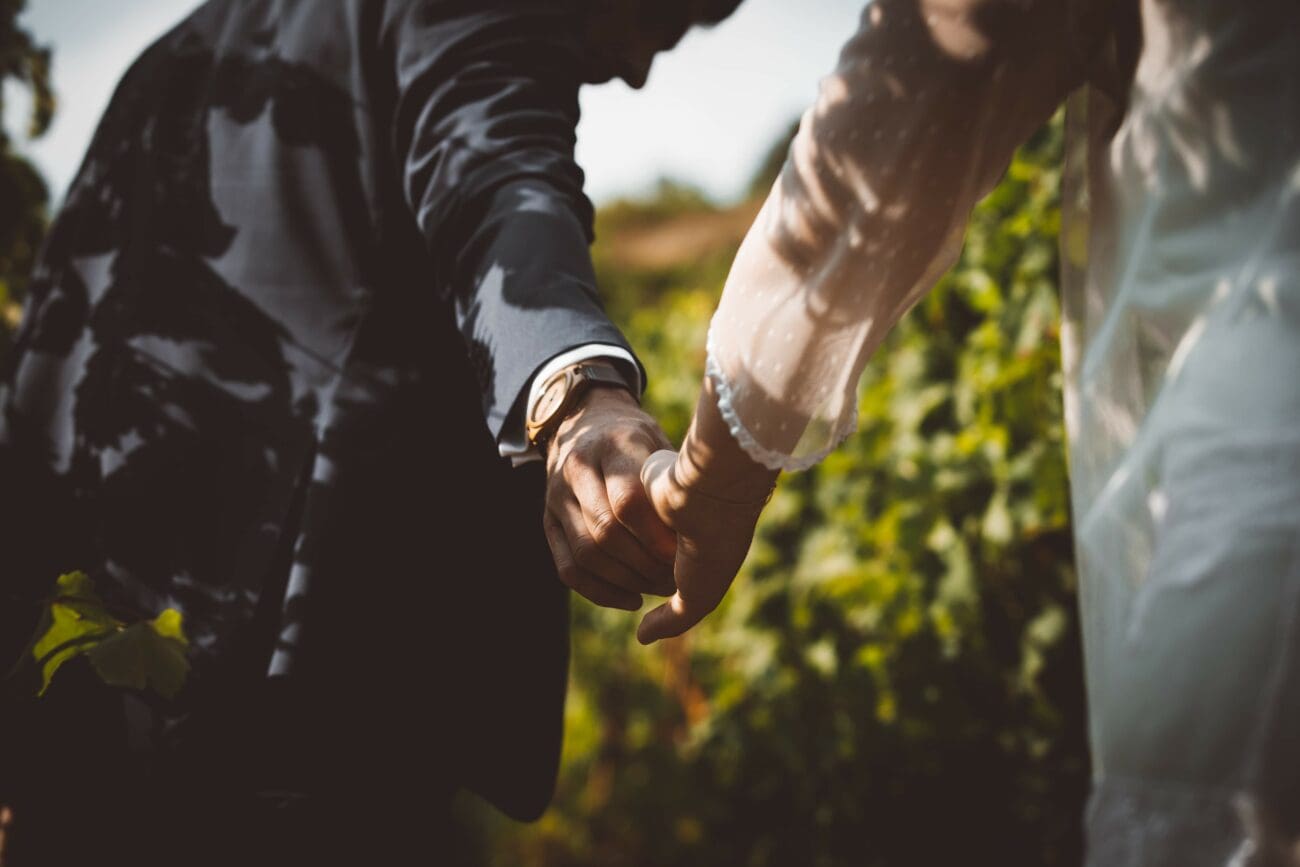 Gros plan sur les mains de jeunes mariés se tenant par la main au cœur d'un vignoble.