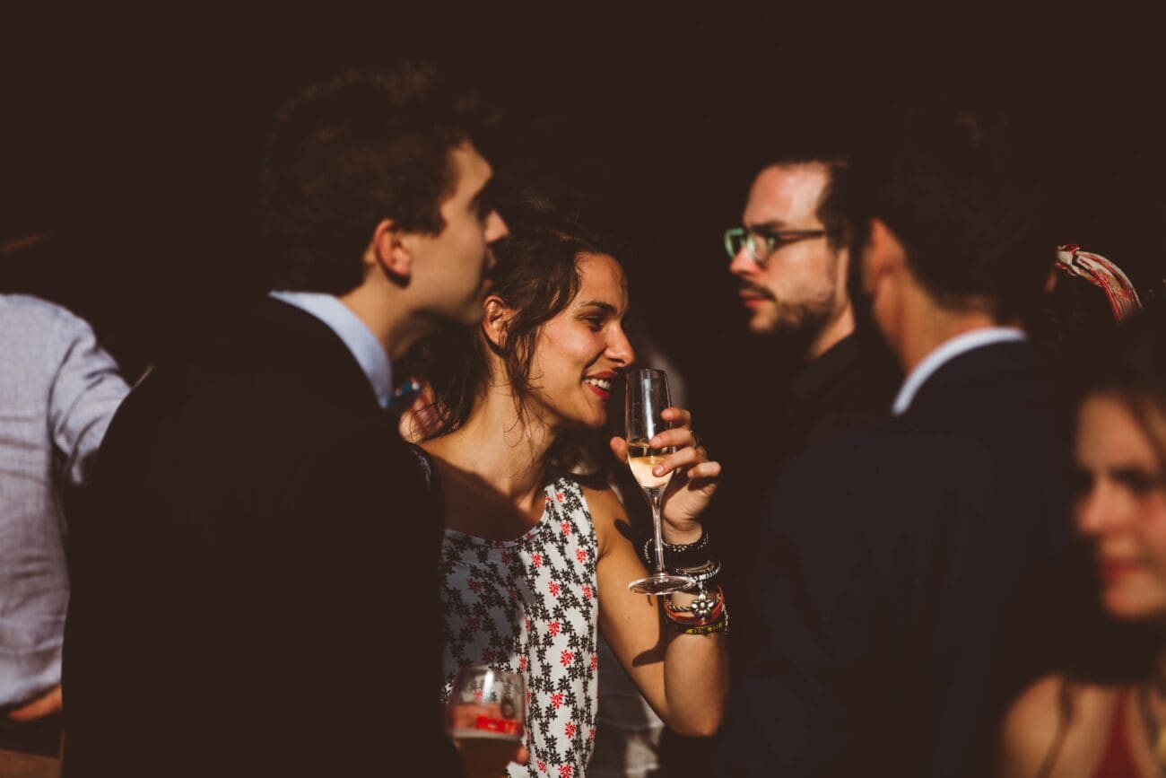Invitée de mariage souriante tenant une flûte de champagne lors d'un cocktail festif en soirée.