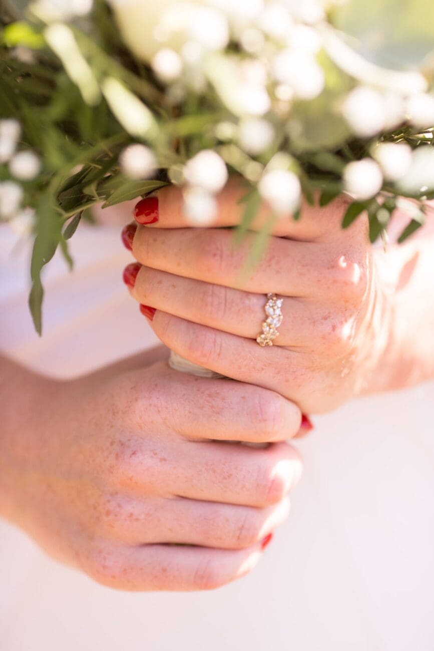 Zoom sur les mains d'une mariée avec son alliance et bouquet de fleurs, illustration de l'élégance et de l'expertise de vins-mariages.net pour les cérémonies à Dijon.