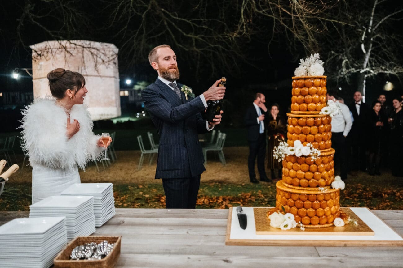 Mariés célébrant avec une bouteille de Champagne devant une pièce montée lors d'une réception de mariage en extérieur