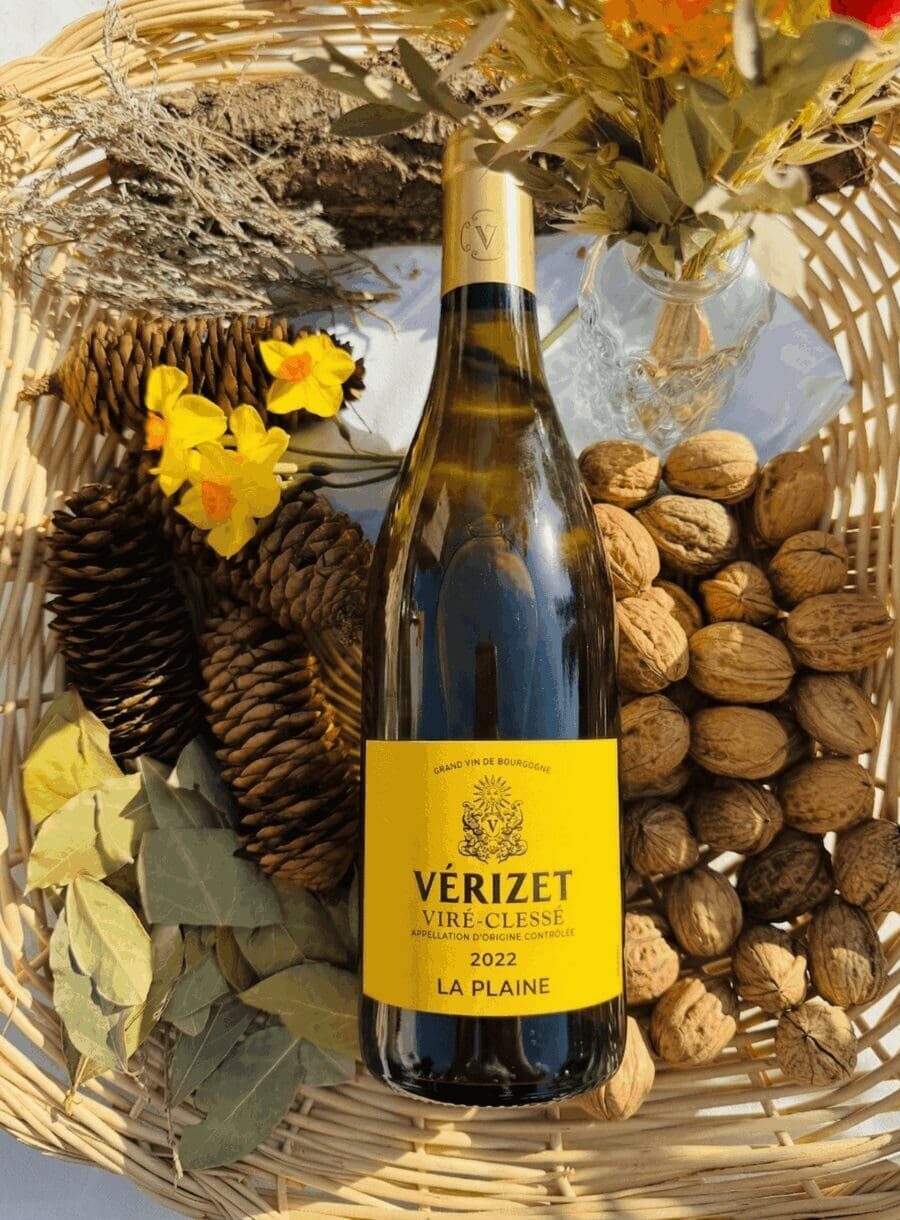 Bouteille de vin blanc Viré-Clessé "La Plaine" 2022 de Vérizet dans un panier en osier avec des noix, des pommes de pin et des fleurs jaunes printanières.