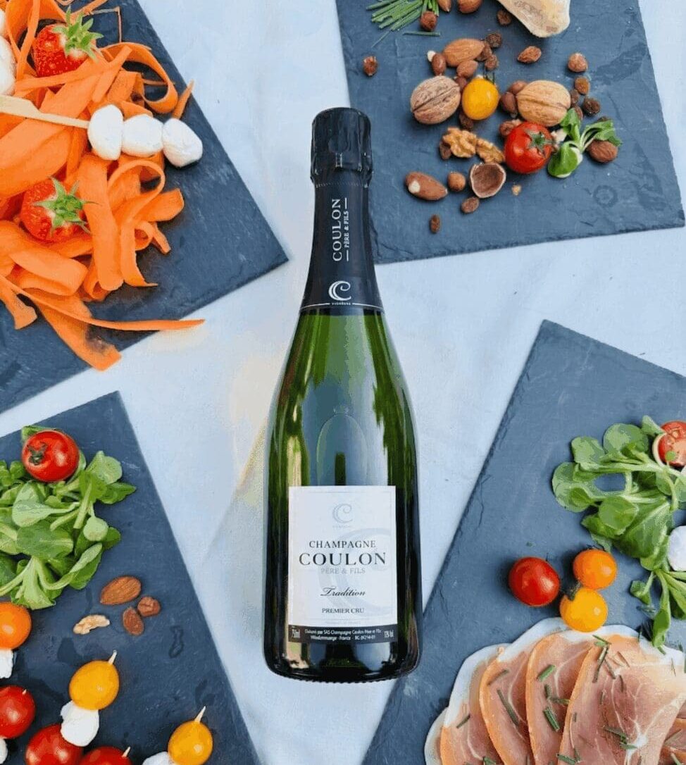 Bouteille de champagne Coulon Brut Tradition entourée d'ardoises apéritives pour un buffet de mariage.