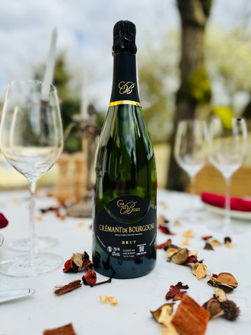 Bouteille de Crémant de Bourgogne Brut Cave de Bissey sur une table dressée avec verres à pied et décor extérieur.