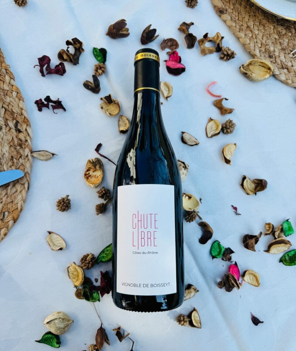Bouteille de vin rouge Côtes-du-Rhône "Chute Libre" 2023 du Vignoble de Boisseyt posée sur une nappe blanche parsemée de pétales de fleurs séchées.