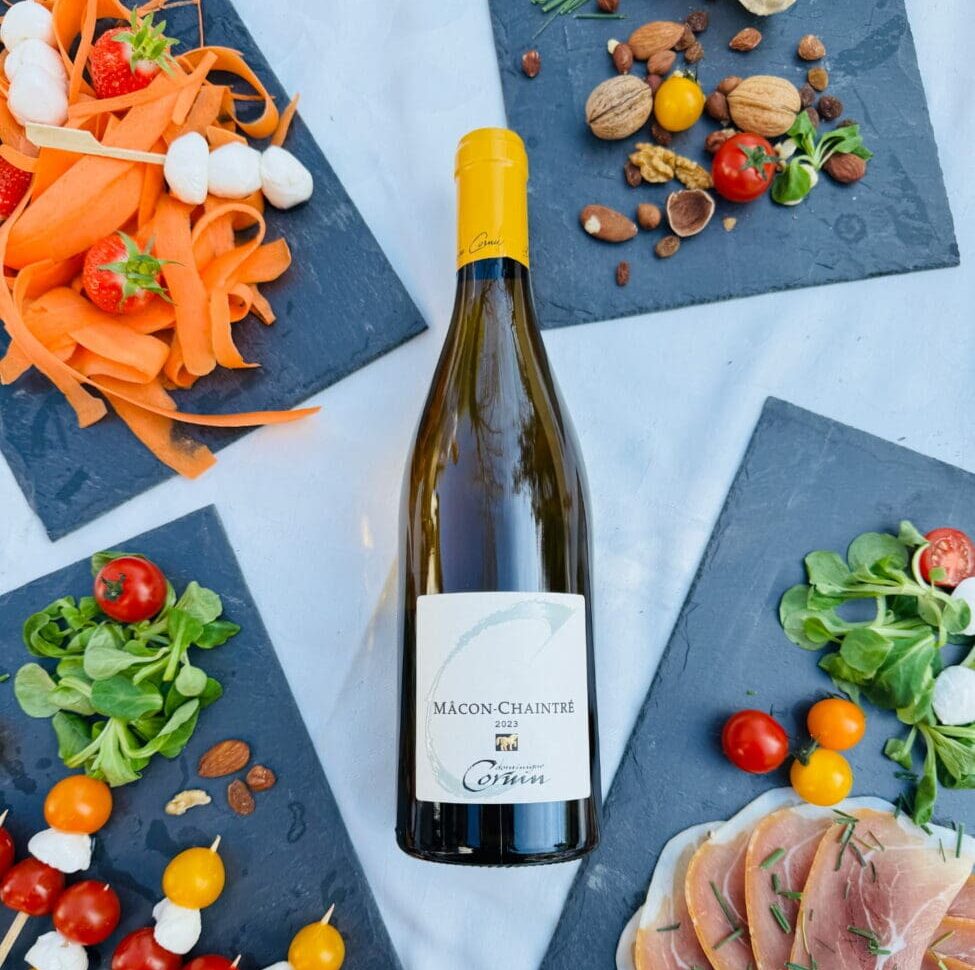 Bouteille de vin blanc Mâcon-Chaintré 2023 du Domaine Cornin entourée d'ardoises de dégustation avec jambon cru, tomates cerises et crudités.