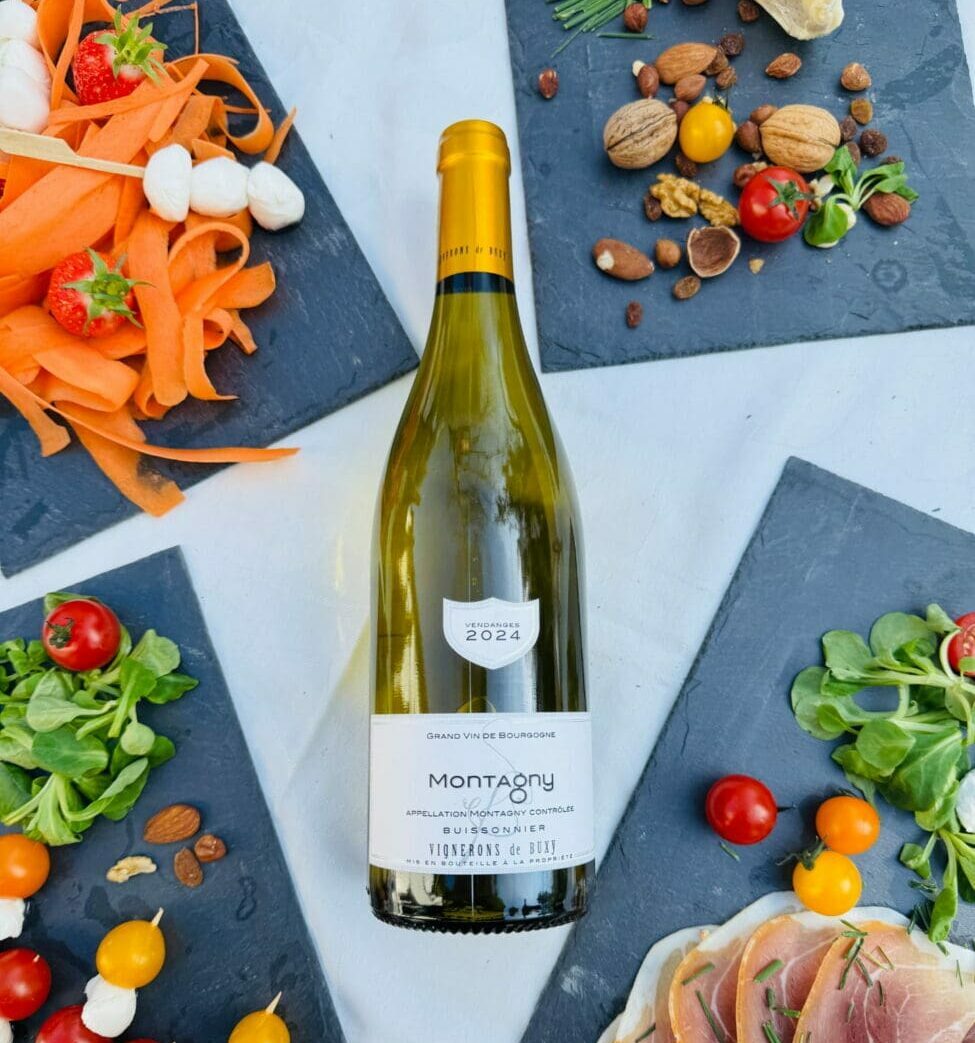 Bouteille de vin blanc Montagny 2024 entourée de planches de dégustation avec charcuterie, crudités et tomates cerises.