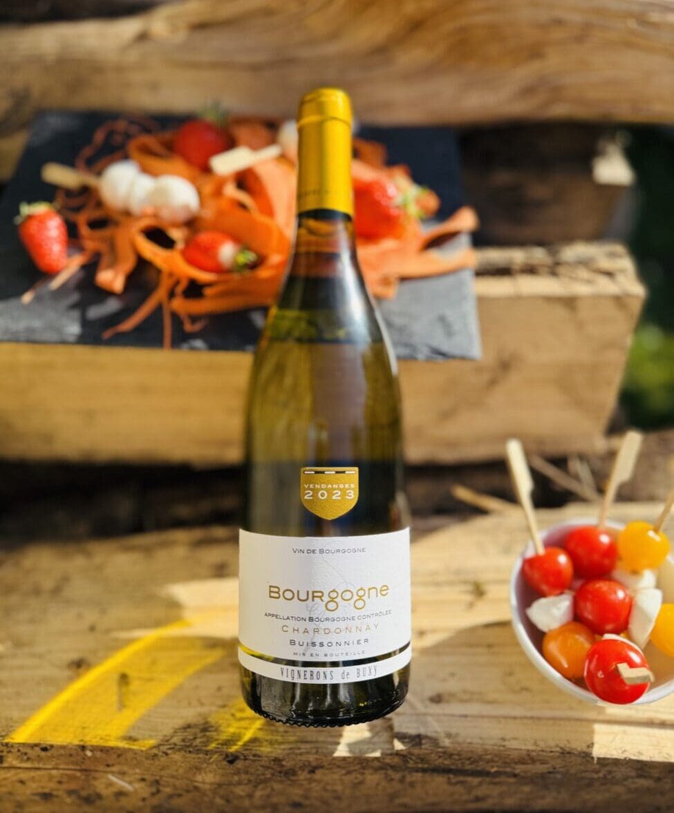 Bouteille de vin blanc Bourgogne Chardonnay Buissonnier 2023 des Vignerons de Buxy sur une caisse en bois avec des brochettes apéritives de tomates et mozzarella.