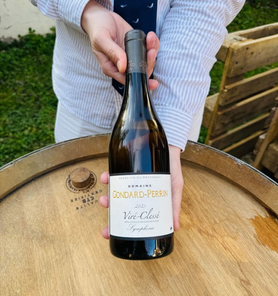 Une personne présente une bouteille de vin blanc Viré-Clessé "Symphonie" 2023 du Domaine Gondard-Perrin au-dessus d'un tonneau en chêne.