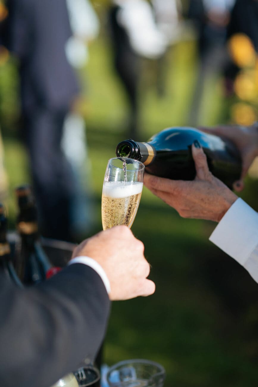 Versement de champagne ou crémant dans une flûte lors d'une réception de mariage en extérieur.