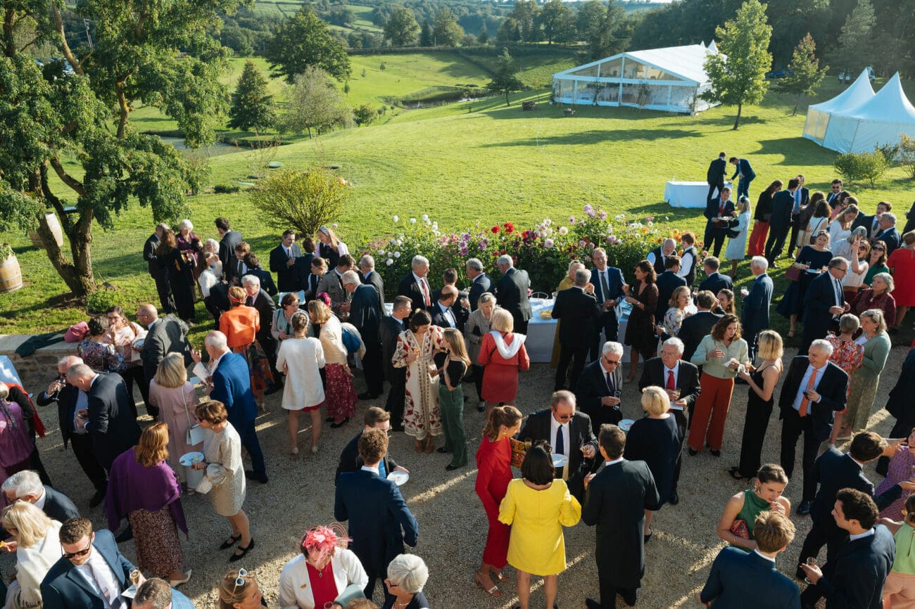 Vin d'honneur de mariage en extérieur avec invités dégustant du vin devant un chapiteau de réception.