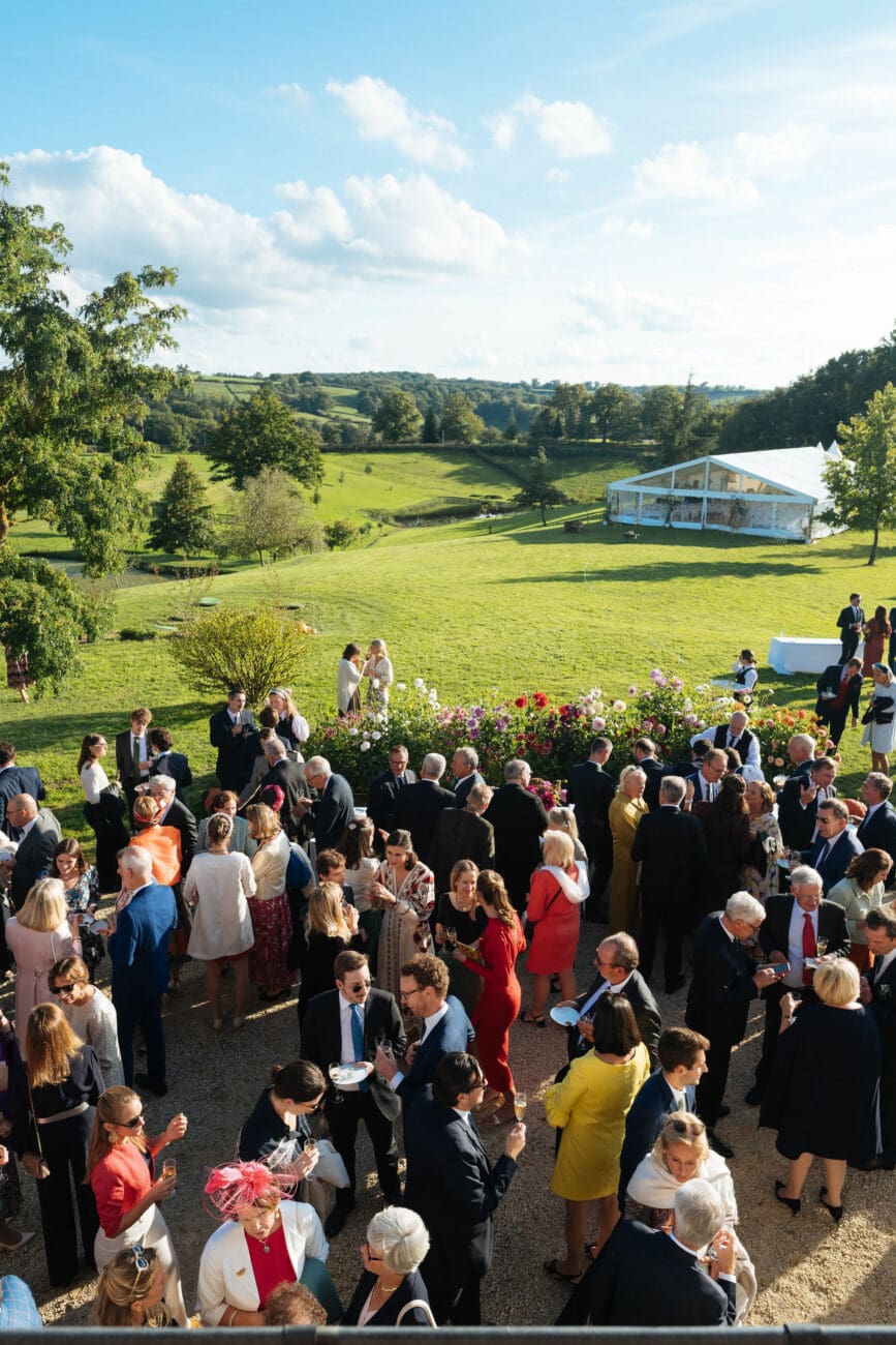 Vue plongeante sur un vin d'honneur de mariage avec de nombreux invités dans un parc avec chapiteau blanc.