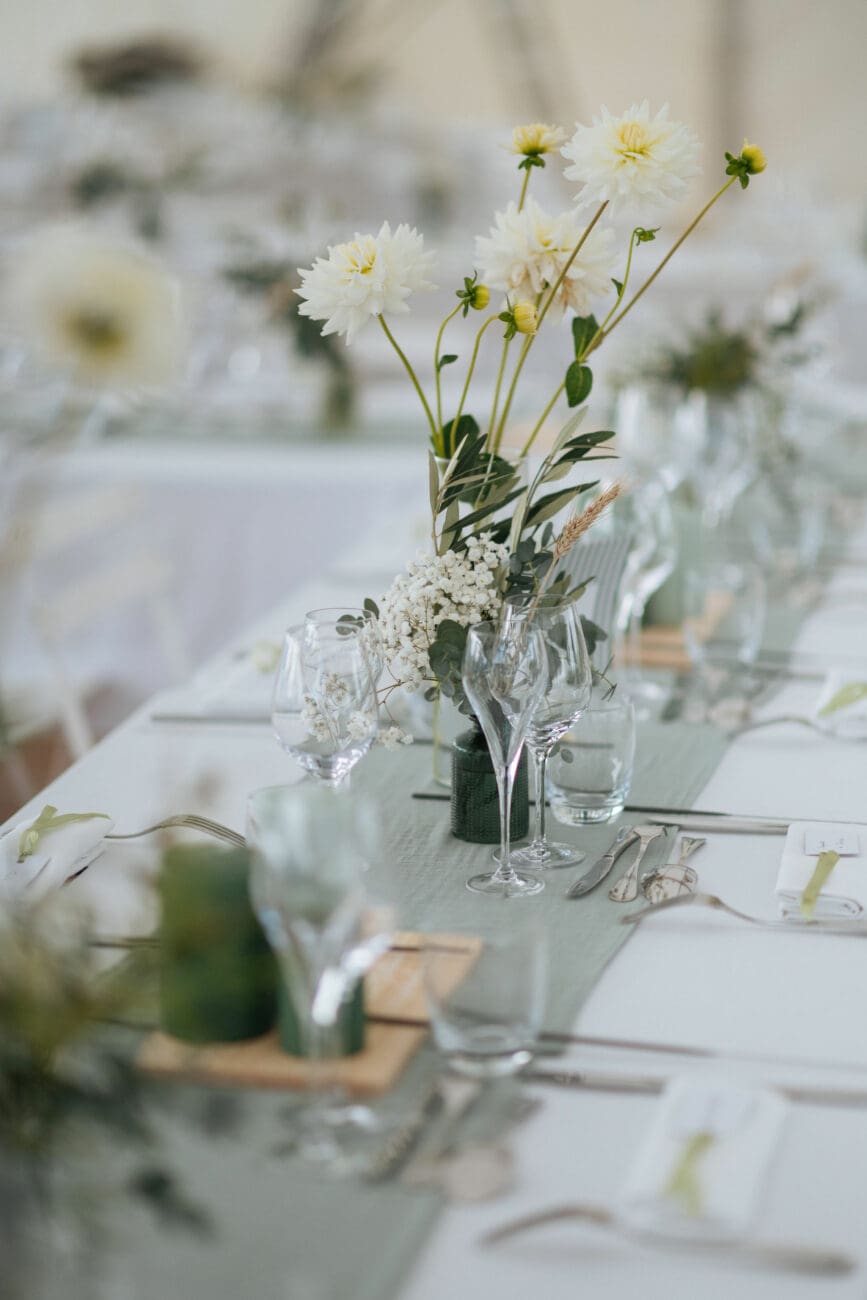 Décoration de table de mariage élégante et champêtre avec fleurs blanches et chemin de table vert d'eau, illustrant l'ambiance idéale pour un accord mets et vins réussi lors du repas de noces.