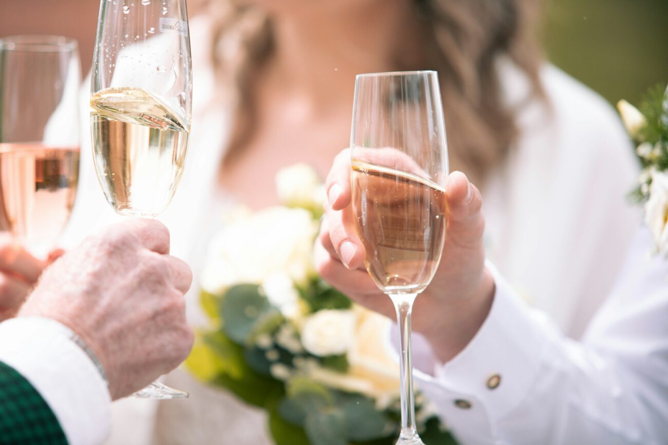 Invités et mariés trinquant avec des flûtes de champagne et de vin rosé lors d'une réception de mariage en plein air.