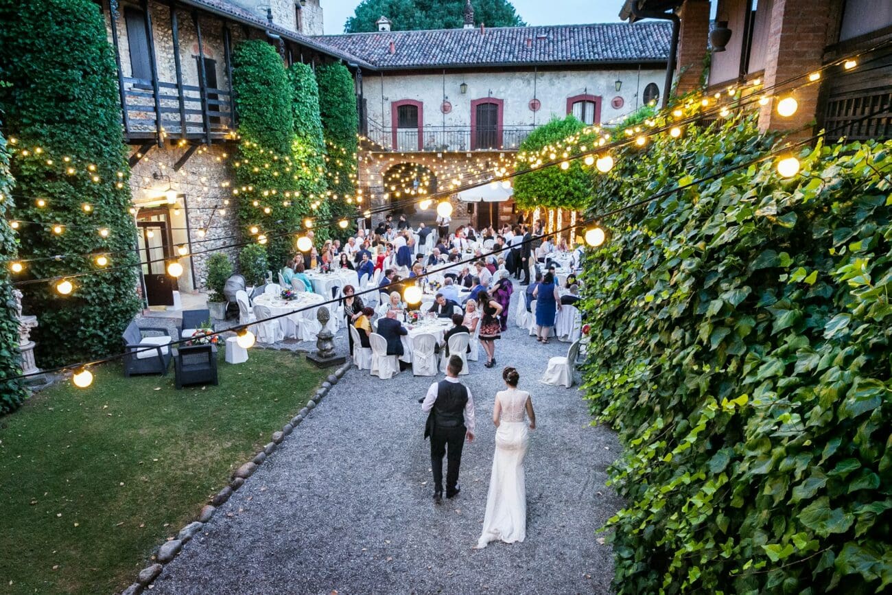 Vue aérienne d'une réception de mariage en soirée dans une cour de château avec des guirlandes lumineuses, des tables dressées et des invités.