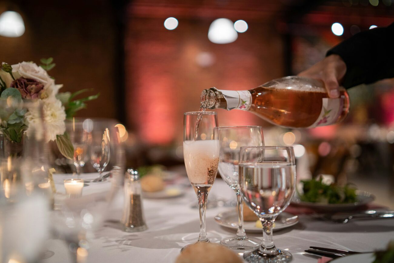 Un serveur verse du vin pétillant rosé dans une flûte sur une table de mariage élégamment dressée avec des fleurs et des bougies.