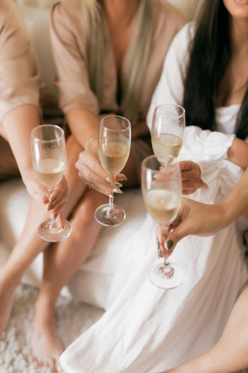 Gros plan de quatre femmes, dont une en robe blanche, tenant des flûtes de champagne et faisant un toast lors d'une célébration de mariage.