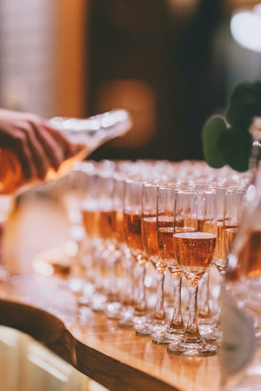 Service de champagne rosé ou crémant pour le vin d'honneur d'un mariage, alignement de flûtes sur un bar en bois.