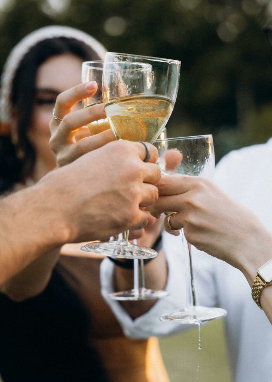 Gros plan sur des invités de mariage trinquant avec des verres de vin blanc lors d'une célébration festif.