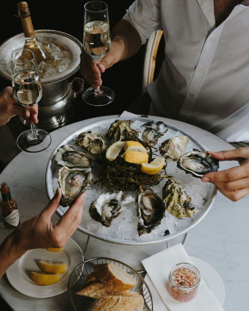 Plateau d'huîtres sur glace avec quartiers de citron, pain et mignonette, accompagné de flûtes de champagne pour une réception de mariage, proposé par vins-mariages.net