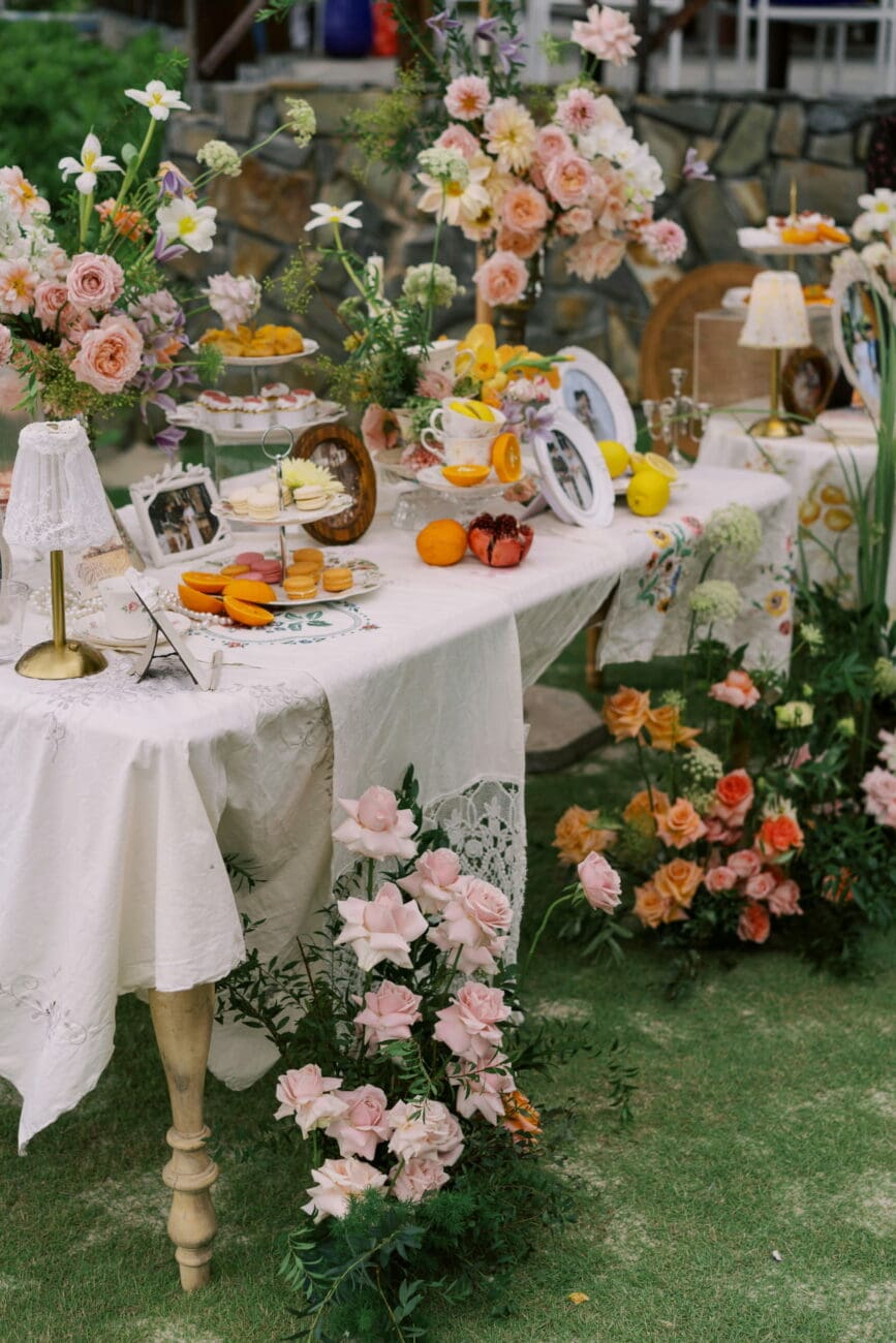 Table de brunch de mariage romantique en extérieur avec décoration florale rose, macarons et agrumes, un cadre idéal pour les vins de vins-mariages.net.