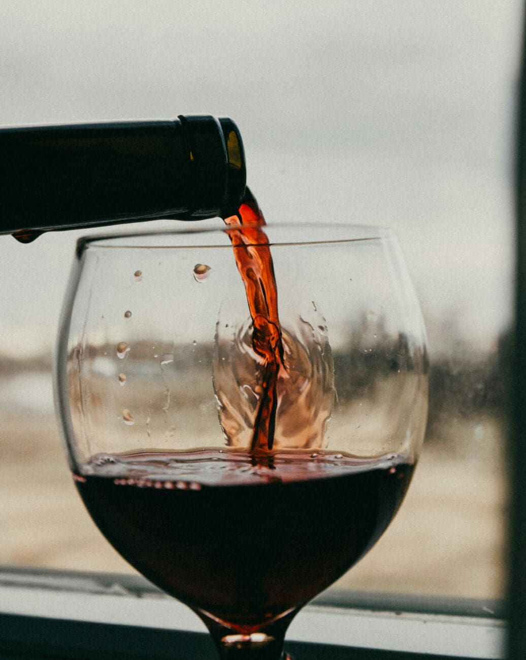 Gros plan sur un vin rouge intense versé dans un verre ballon, capturé avec un effet de mouvement et des reflets de lumière.