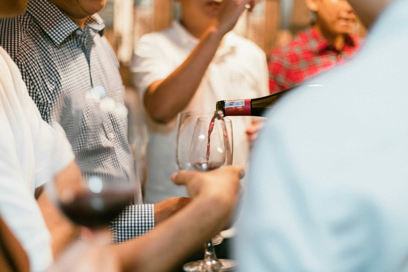 Service d'un vin rouge dans un verre tenu par un invité lors d'une séance de dégustation conviviale en groupe.