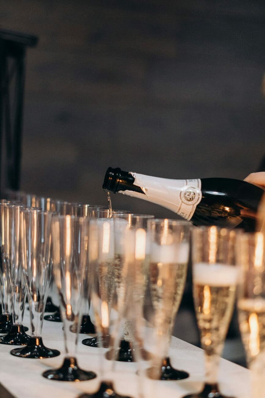Un serveur remplit une rangée de flûtes à champagne élégantes lors d'une réception de mariage.