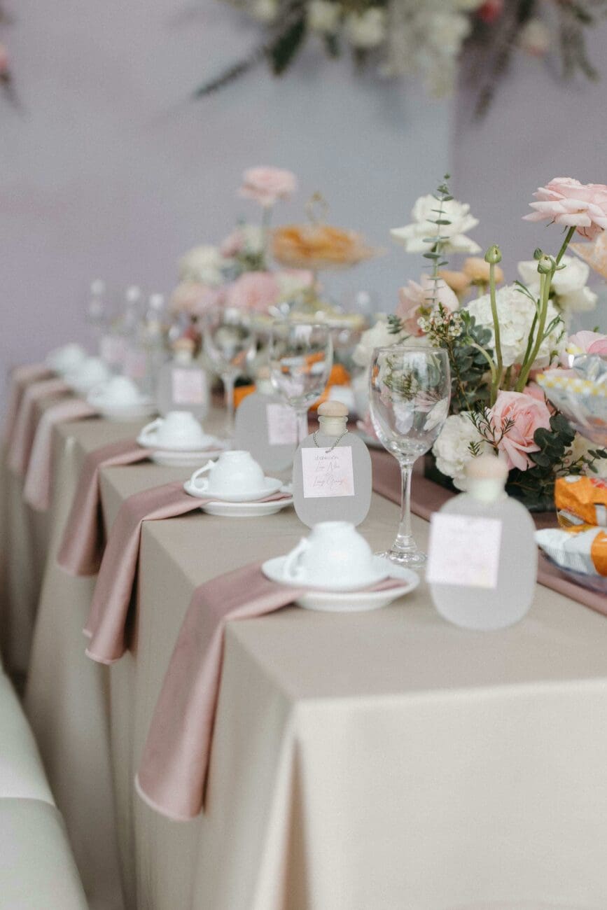 Décoration de table de mariage élégante avec nappe rose poudré, bouquets floraux, verres à pied et petits cadeaux invités, une ambiance vins-mariages.net.