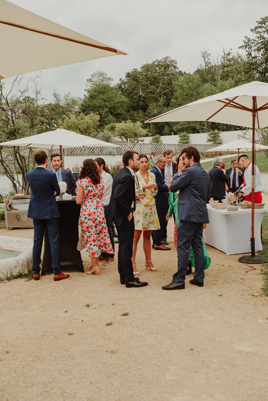 Invités en tenue élégante discutant lors d'un cocktail de mariage en extérieur sous des parasols blancs.